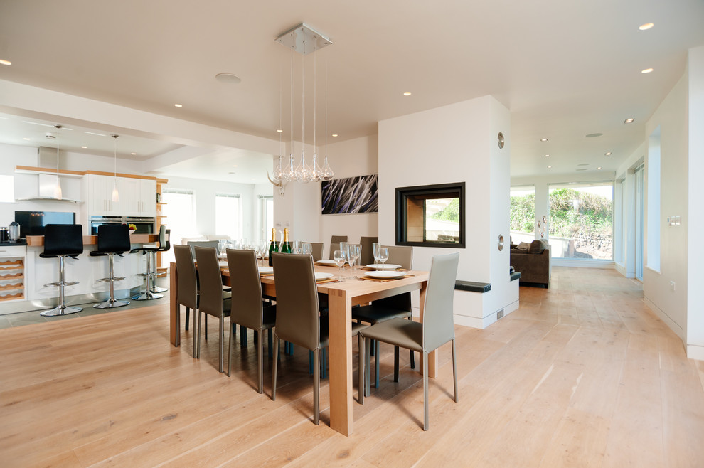 Inspiration pour une très grande salle à manger ouverte sur la cuisine design avec un mur blanc, un sol en bois brun, un poêle à bois et un manteau de cheminée en plâtre.