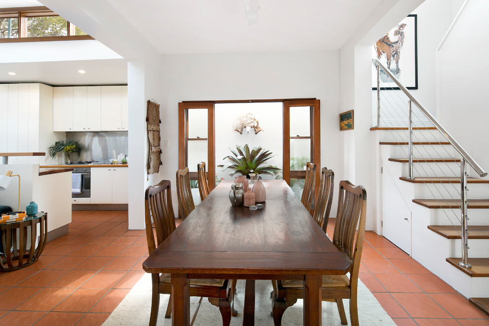 Foto di una sala da pranzo aperta verso la cucina con pareti bianche, pavimento in terracotta e nessun camino