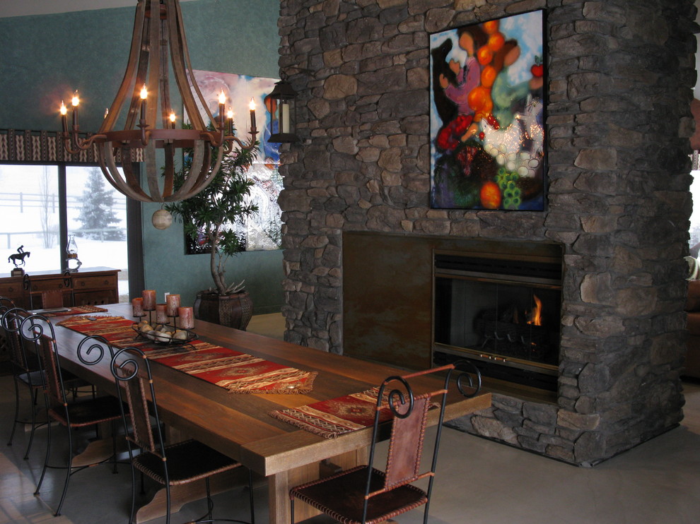 Esempio di una sala da pranzo aperta verso la cucina stile rurale di medie dimensioni con pareti grigie, pavimento in cemento, camino bifacciale e cornice del camino in pietra