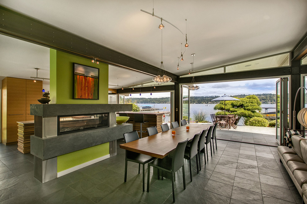 Foto di una sala da pranzo aperta verso la cucina minimalista con pareti verdi, pavimento in ardesia e camino bifacciale