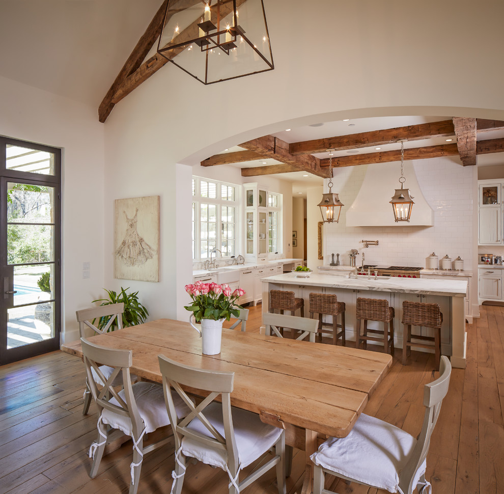 Cette photo montre une salle à manger ouverte sur la cuisine chic avec un mur blanc, un sol en bois brun et éclairage.