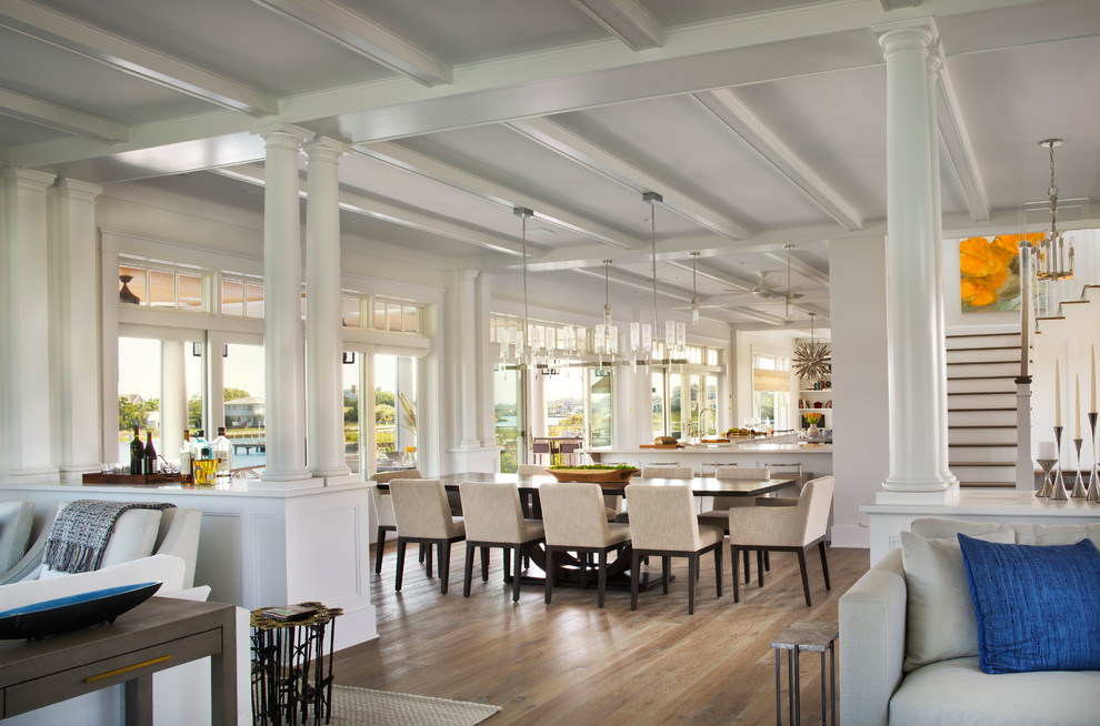 Cette image montre une grande salle à manger ouverte sur le salon marine avec un mur blanc et un sol en bois brun.