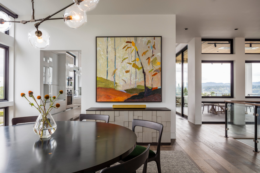 Cette image montre une grande salle à manger ouverte sur le salon minimaliste avec un mur blanc, un sol en bois brun, aucune cheminée et un sol marron.