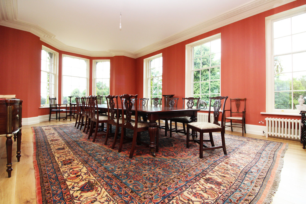 Réalisation d'une très grande salle à manger tradition fermée avec un mur rose, un sol en bois brun, une cheminée standard et un manteau de cheminée en plâtre.