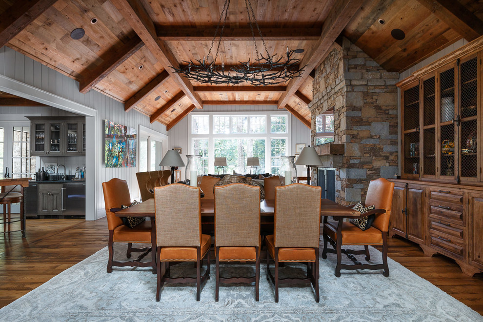 This is an example of a rustic dining room in Other with grey walls, dark hardwood flooring, a standard fireplace, a stone fireplace surround and feature lighting.