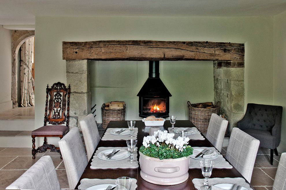 Cette photo montre une grande salle à manger nature avec un sol en calcaire, un poêle à bois, un manteau de cheminée en pierre et un mur vert.