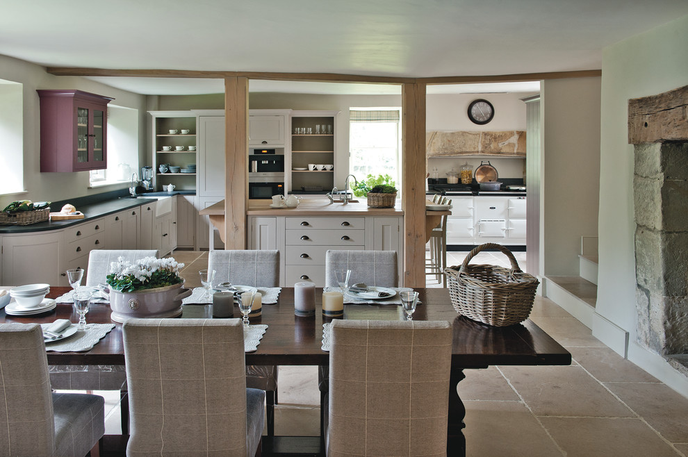 На фото: большая кухня-столовая в стиле кантри с полом из известняка, белыми стенами, стандартным камином и фасадом камина из камня