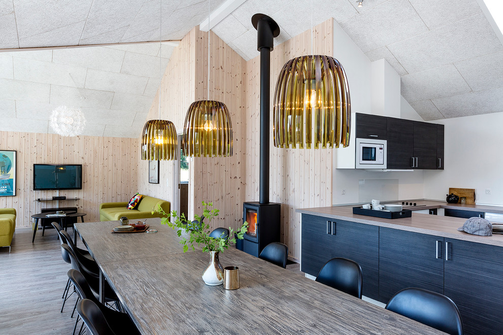 Aménagement d'une grande salle à manger ouverte sur la cuisine scandinave avec un mur beige, parquet clair, un poêle à bois et un manteau de cheminée en métal.