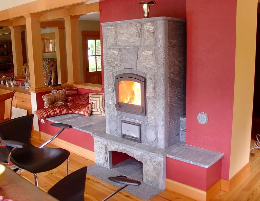 Exemple d'une salle à manger ouverte sur la cuisine éclectique de taille moyenne avec un mur rouge, parquet clair, un poêle à bois et un manteau de cheminée en pierre.