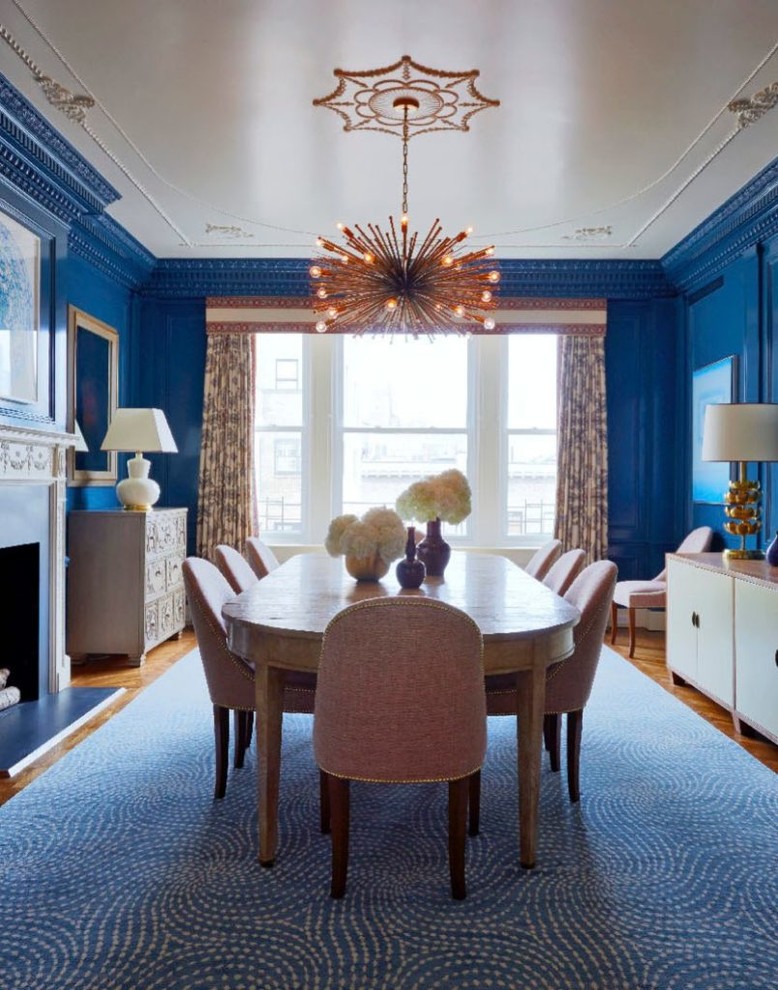 Ispirazione per una sala da pranzo tradizionale con pareti blu, pavimento in legno massello medio, camino classico, cornice del camino in intonaco e pavimento beige