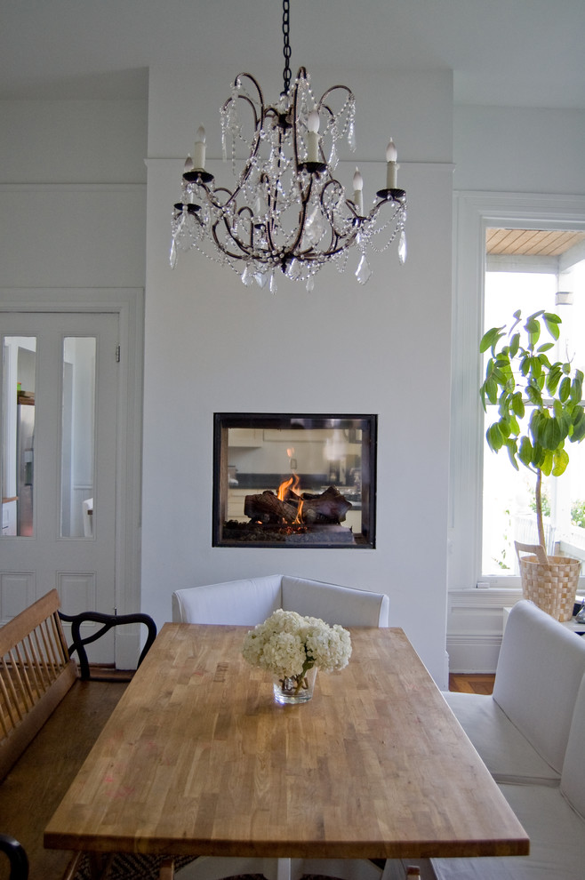 Example of an eclectic light wood floor kitchen/dining room combo design in San Francisco with white walls, a two-sided fireplace and a metal fireplace