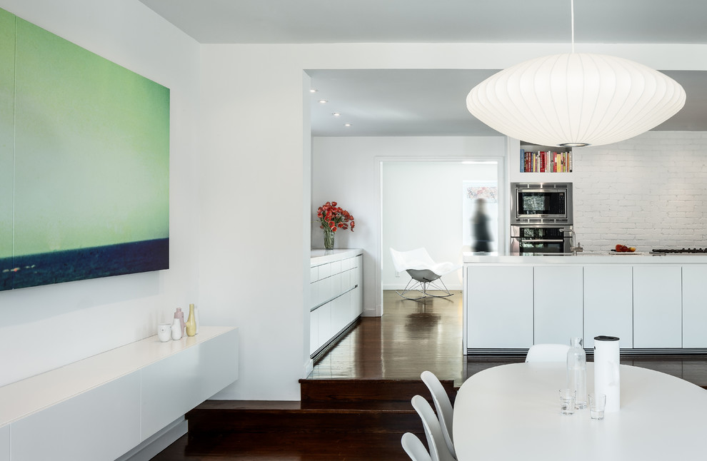 Immagine di una sala da pranzo aperta verso il soggiorno minimalista di medie dimensioni con parquet scuro, pareti bianche e nessun camino
