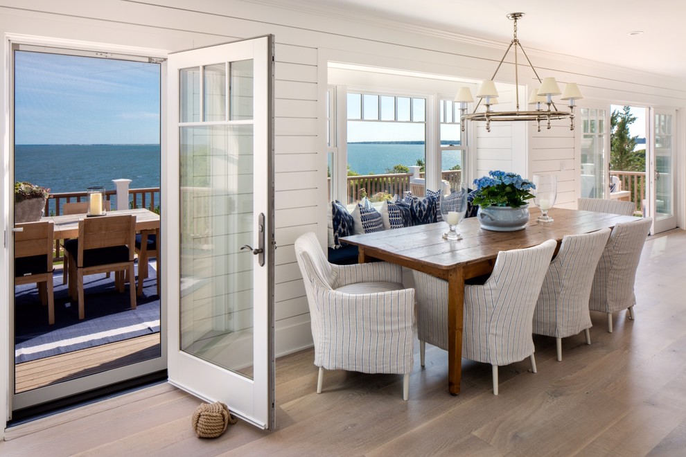 Aménagement d'une salle à manger ouverte sur la cuisine bord de mer avec un mur blanc et un sol en bois brun.