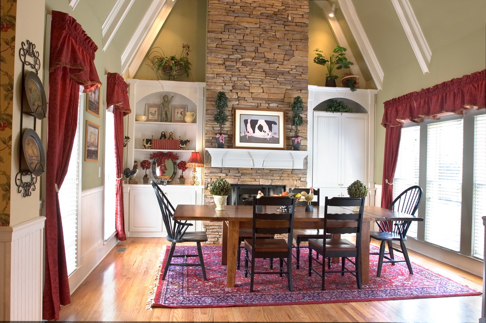 Réalisation d'une grande salle à manger ouverte sur la cuisine champêtre avec un mur vert, parquet clair, un manteau de cheminée en pierre et cheminée suspendue.