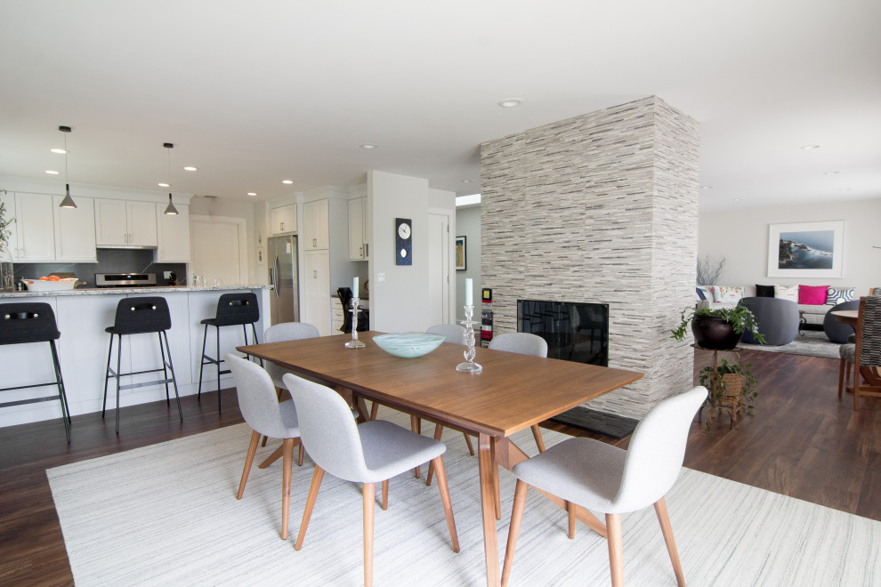 Cette photo montre une salle à manger ouverte sur la cuisine moderne de taille moyenne avec un mur gris, un sol en vinyl, une cheminée double-face et un sol marron.
