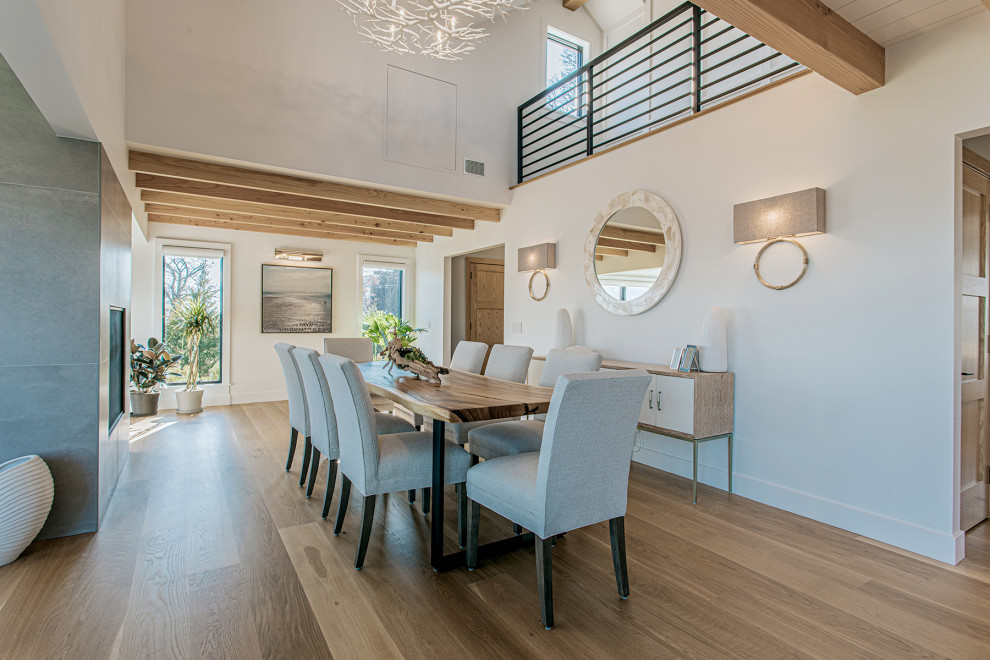 Country open plan dining room in New York with a two-sided fireplace, a concrete fireplace surround, white walls, medium hardwood flooring and brown floors.