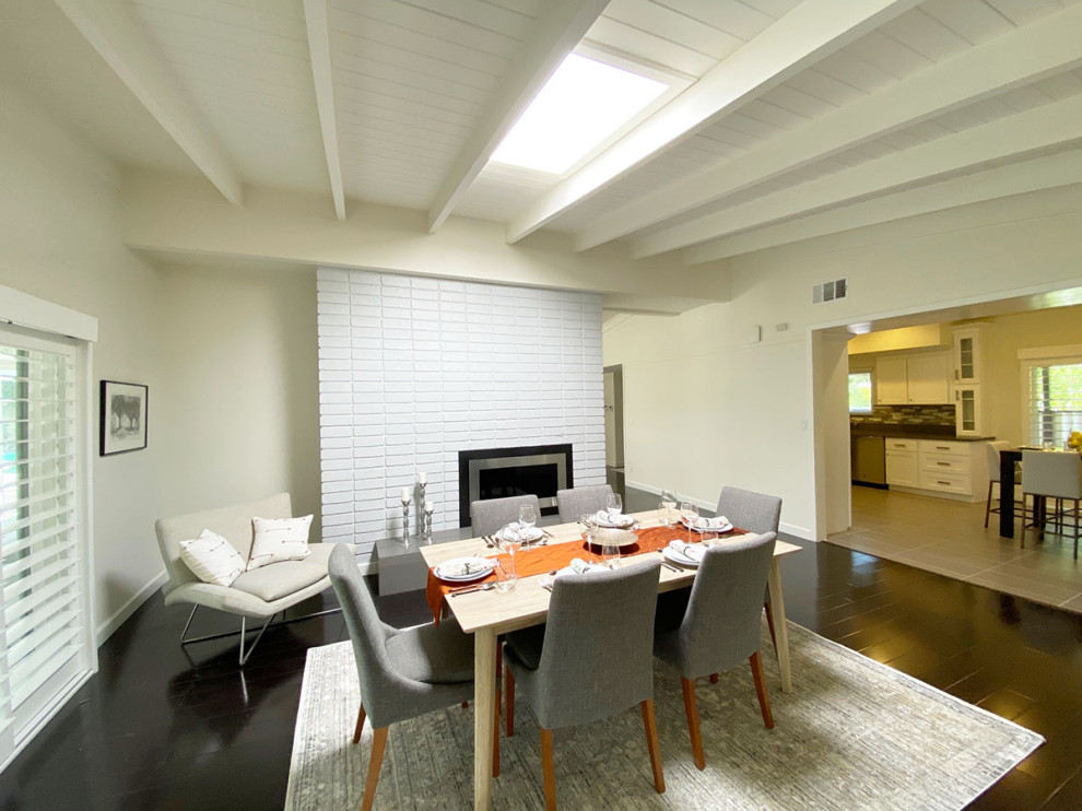 Пример оригинального дизайна: гостиная-столовая среднего размера в стиле модернизм с белыми стенами, полом из ламината, двусторонним камином, фасадом камина из кирпича, черным полом и сводчатым потолком