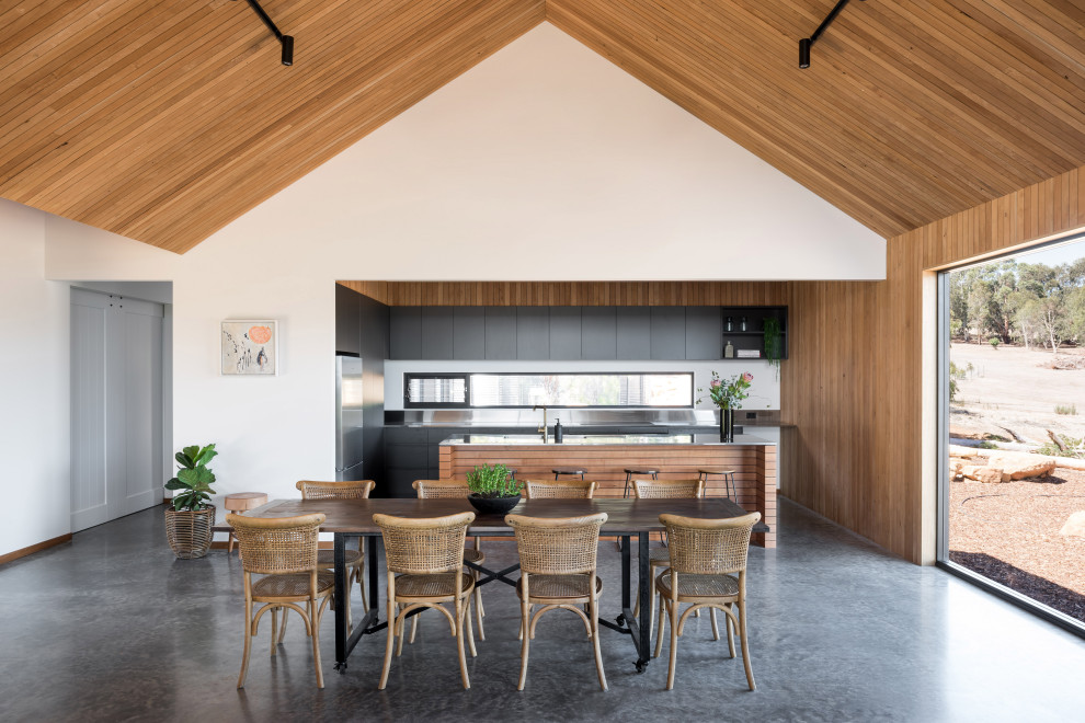 Cette image montre une salle à manger ouverte sur le salon rustique en bois avec un mur blanc, sol en béton ciré, un sol gris, un plafond voûté et un plafond en bois.