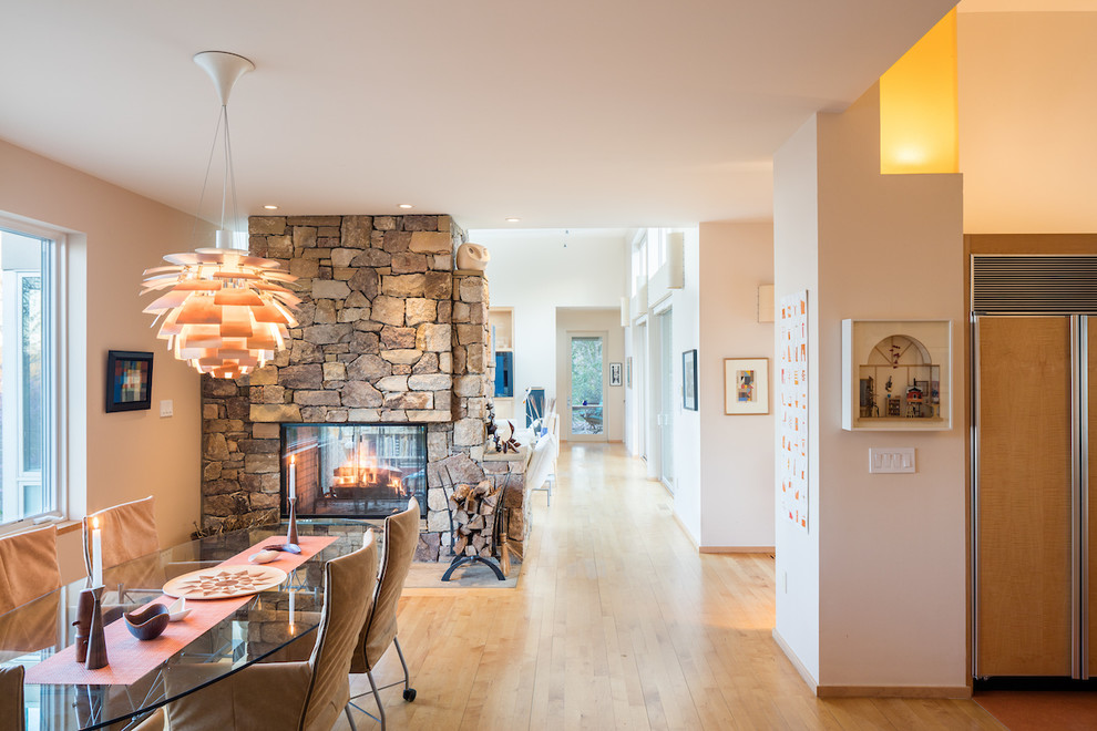 Ispirazione per una sala da pranzo aperta verso la cucina moderna di medie dimensioni con pareti beige, parquet chiaro, camino bifacciale e cornice del camino in pietra