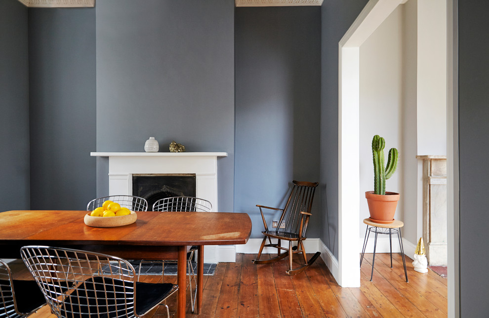 Ispirazione per una sala da pranzo minimalista chiusa con pareti grigie, pavimento in legno massello medio, camino classico e cornice del camino in pietra