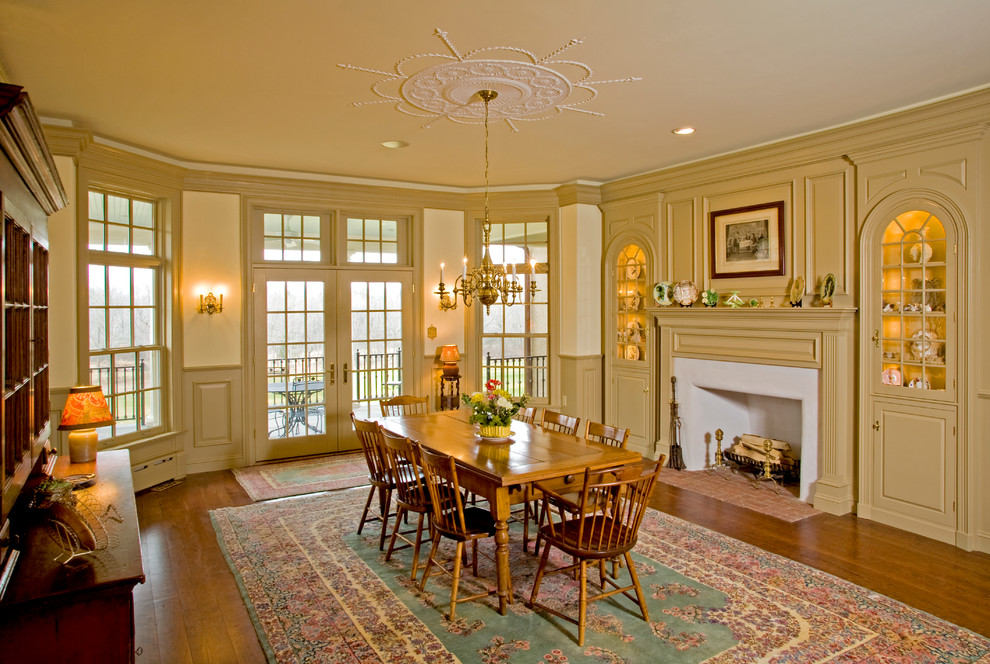 Стильный дизайн: столовая в классическом стиле с желтыми стенами, паркетным полом среднего тона и стандартным камином - последний тренд