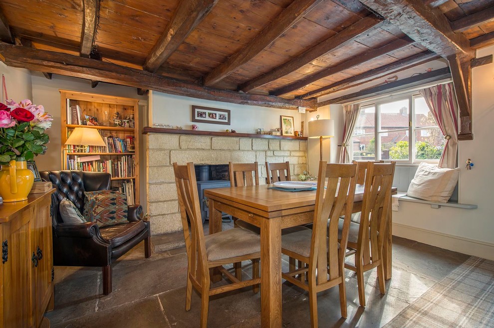 Foto di una piccola sala da pranzo country chiusa con pareti beige, pavimento in ardesia, stufa a legna e cornice del camino in pietra