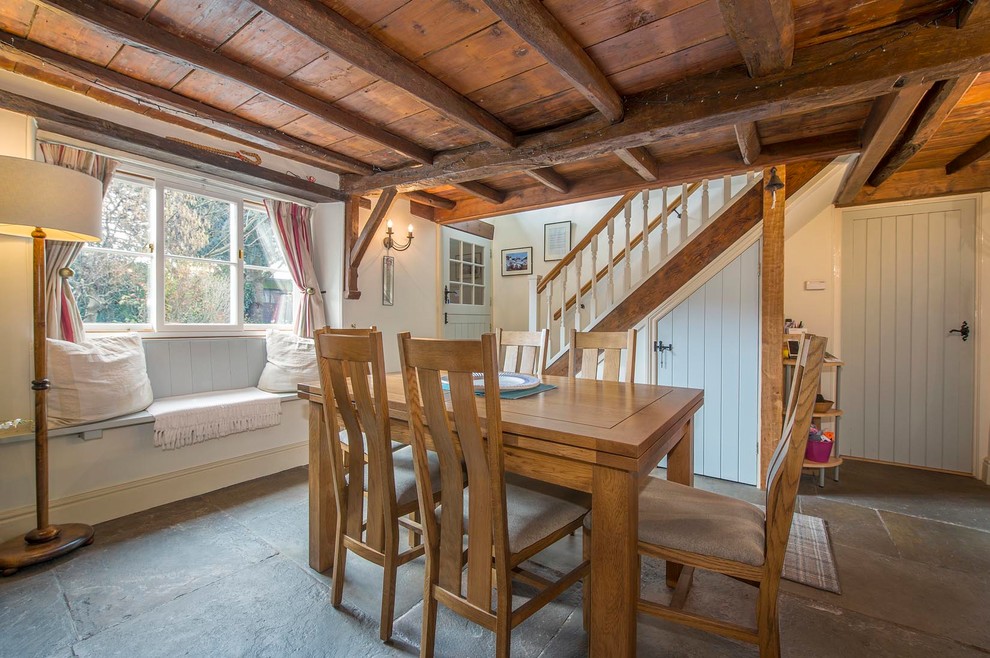 Cette photo montre une petite salle à manger nature fermée avec un mur beige, un sol en ardoise, un poêle à bois et un manteau de cheminée en pierre.