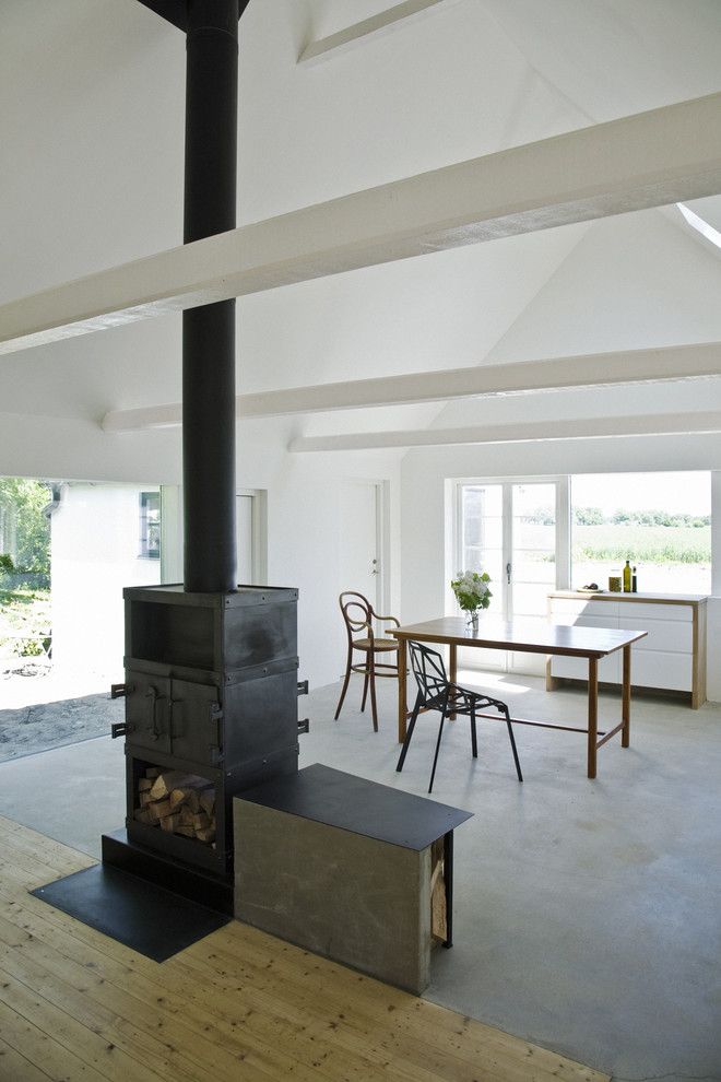Example of a danish concrete floor dining room design in Copenhagen with a wood stove