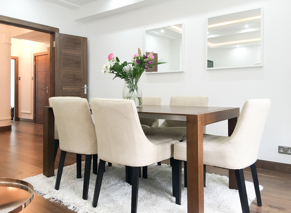 This is an example of a large modern dining room in London with white walls, medium hardwood flooring, a standard fireplace and a stone fireplace surround.