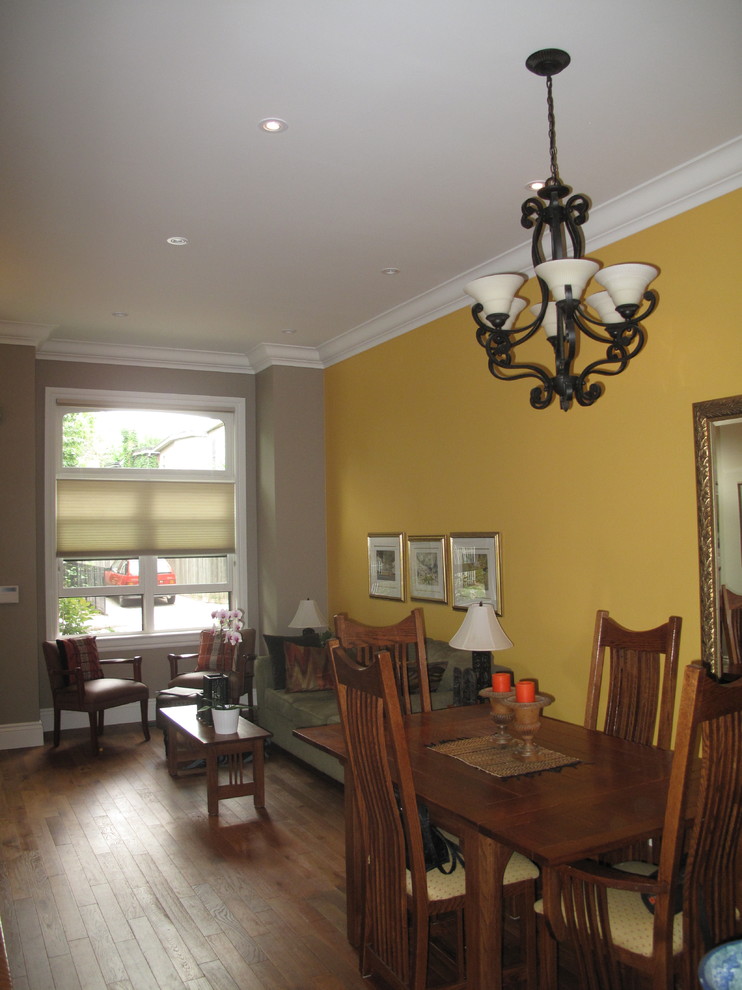 Immagine di una piccola sala da pranzo aperta verso il soggiorno tradizionale con pareti gialle, pavimento in legno massello medio e nessun camino