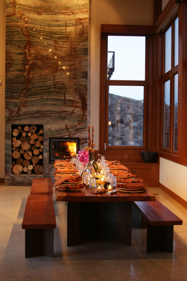 Exemple d'une salle à manger ouverte sur le salon tendance avec un mur beige, un sol en calcaire, une cheminée standard et un manteau de cheminée en pierre.