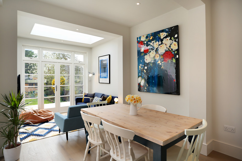 Classic open plan dining room in London with white walls, light hardwood flooring, brown floors and feature lighting.