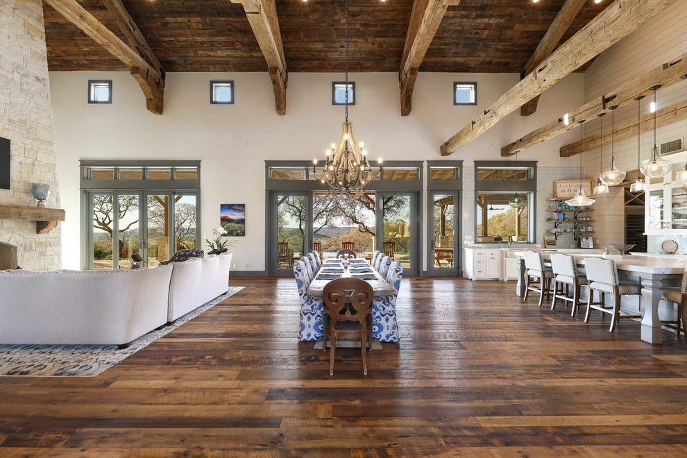 Immagine di un'ampia sala da pranzo aperta verso la cucina rustica con pareti beige, pavimento in legno massello medio, camino bifacciale, cornice del camino in pietra e pavimento marrone