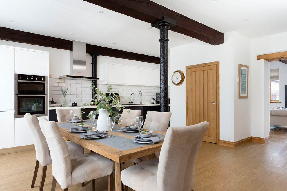 Immagine di una sala da pranzo aperta verso la cucina country con pareti bianche, parquet chiaro e pavimento marrone