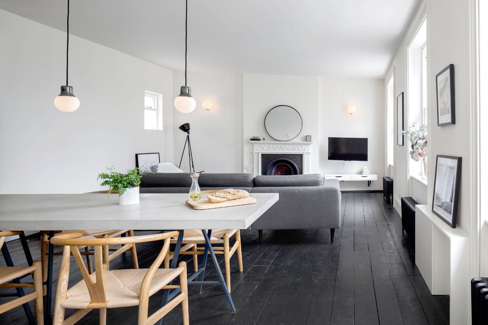 Cette photo montre une salle à manger ouverte sur le salon tendance de taille moyenne avec un mur blanc, parquet foncé, un sol noir, une cheminée standard et un manteau de cheminée en plâtre.