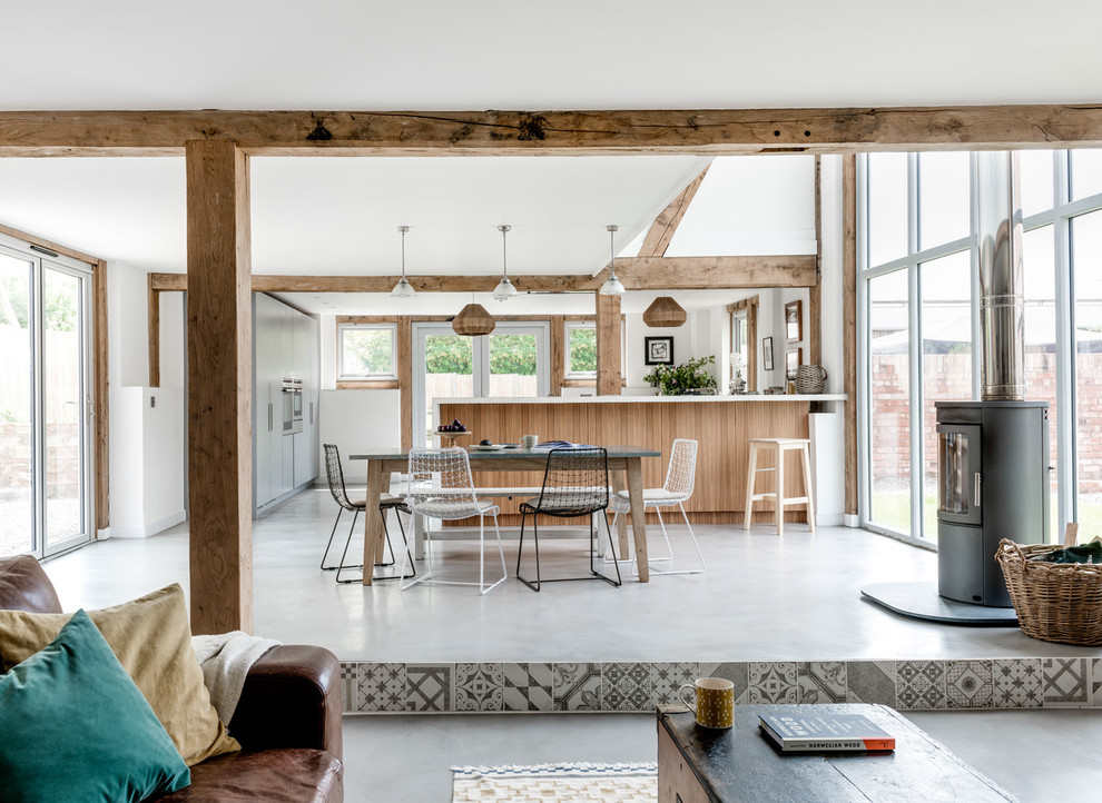 Réalisation d'une salle à manger ouverte sur le salon champêtre avec un mur blanc, un poêle à bois, un manteau de cheminée en métal et un sol gris.