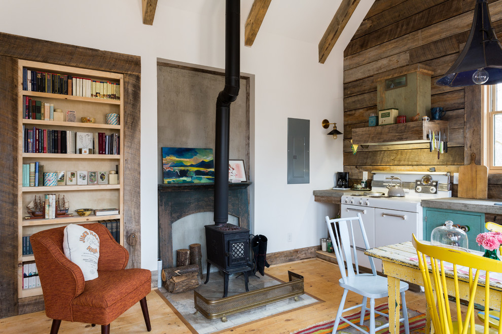 Aménagement d'une petite salle à manger ouverte sur le salon campagne avec un mur blanc, parquet clair, un poêle à bois et un manteau de cheminée en métal.