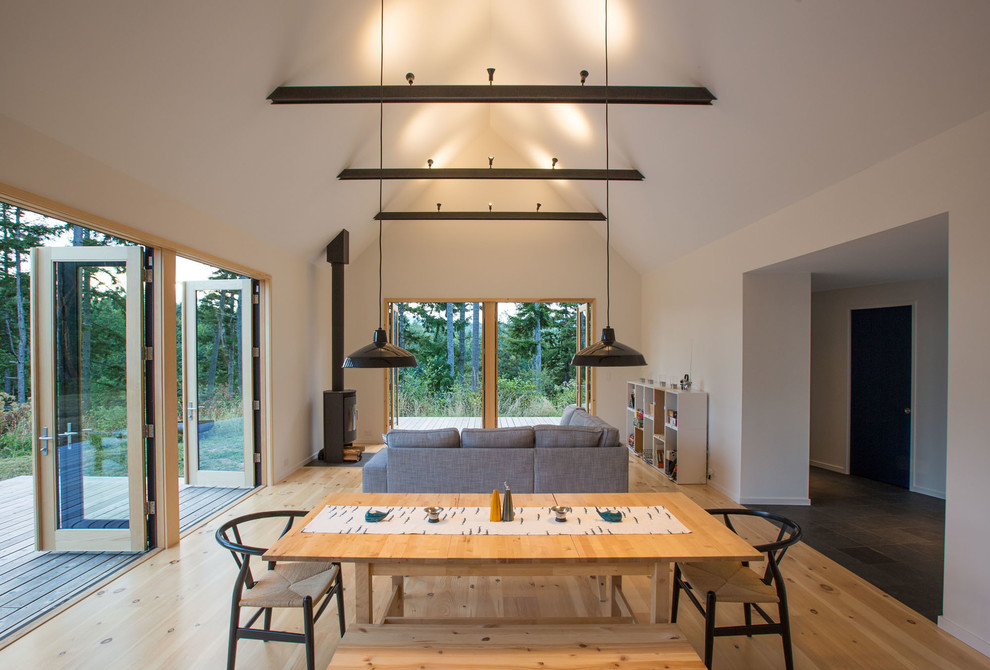 Idée de décoration pour une petite salle à manger ouverte sur le salon chalet avec un mur blanc, parquet clair et un poêle à bois.
