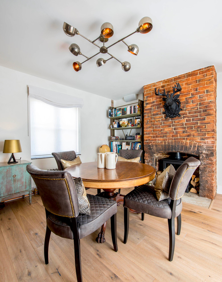 Inspiration for an eclectic dining room in Hampshire with white walls, light hardwood flooring, a standard fireplace, a brick fireplace surround and brown floors.