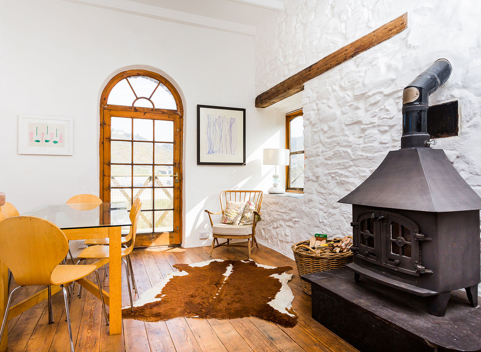 Design ideas for a rural dining room in Cornwall with white walls, medium hardwood flooring and a wood burning stove.