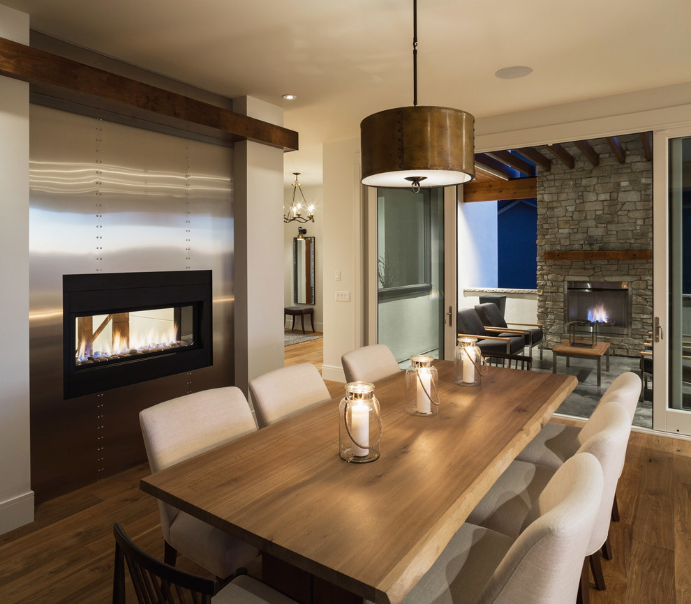 Idée de décoration pour une salle à manger design avec un mur beige, un sol en bois brun, une cheminée double-face et un manteau de cheminée en métal.