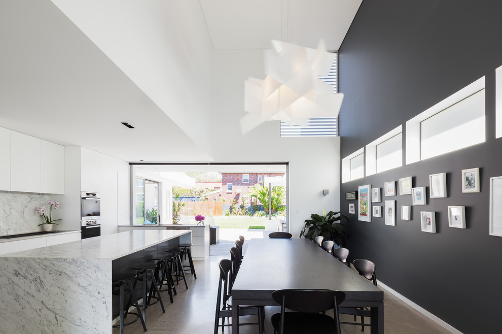 На фото: огромная кухня-столовая в современном стиле с бетонным полом, белыми стенами и серым полом без камина с