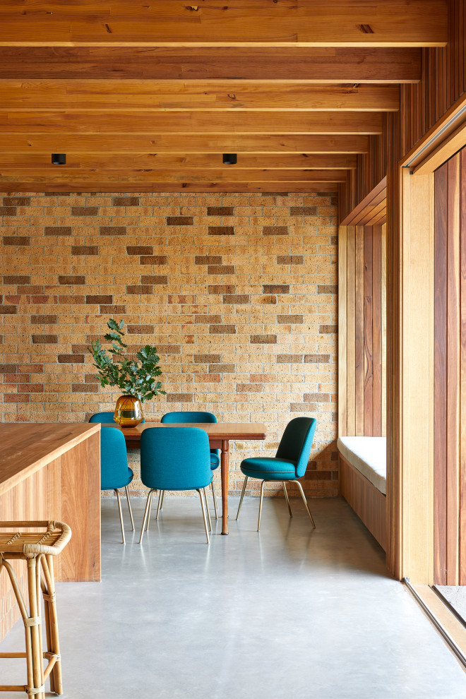 Ispirazione per una sala da pranzo aperta verso la cucina country di medie dimensioni con pareti marroni, pavimento in cemento, pavimento grigio, travi a vista e pareti in mattoni