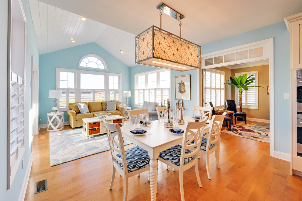 Exemple d'une salle à manger ouverte sur le salon bord de mer avec un mur bleu, un sol en bois brun et éclairage.