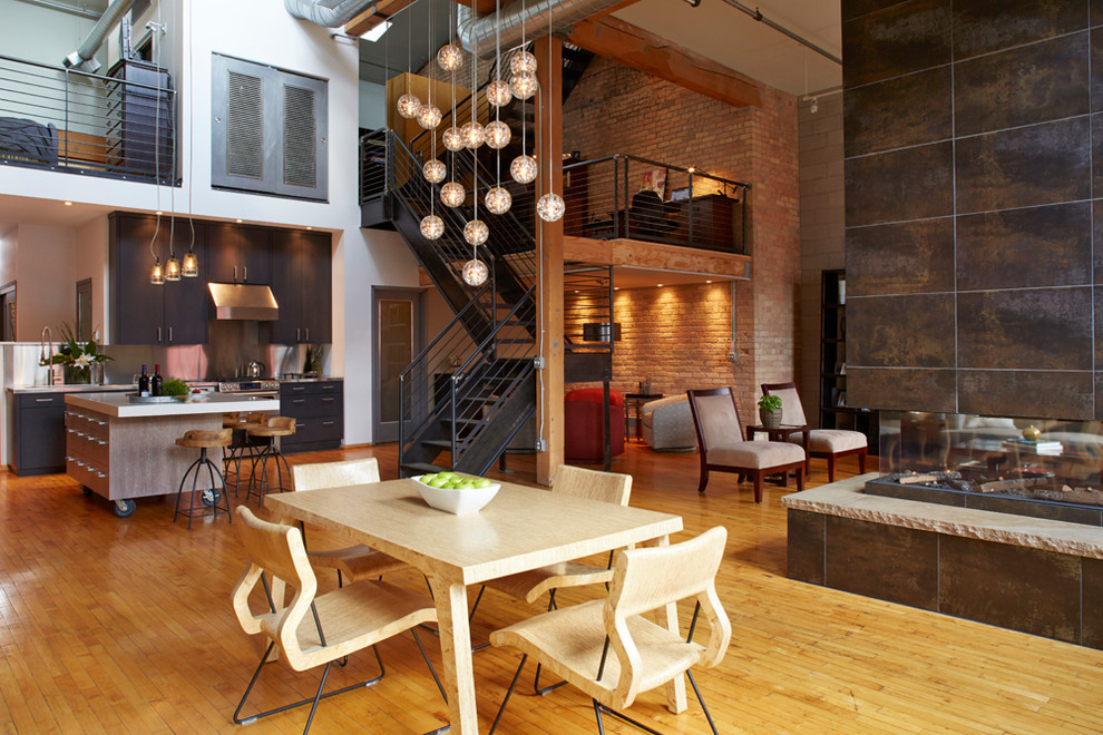 Idée de décoration pour une salle à manger ouverte sur le salon urbaine de taille moyenne avec un sol en bois brun, une cheminée double-face, un manteau de cheminée en métal et un sol marron.