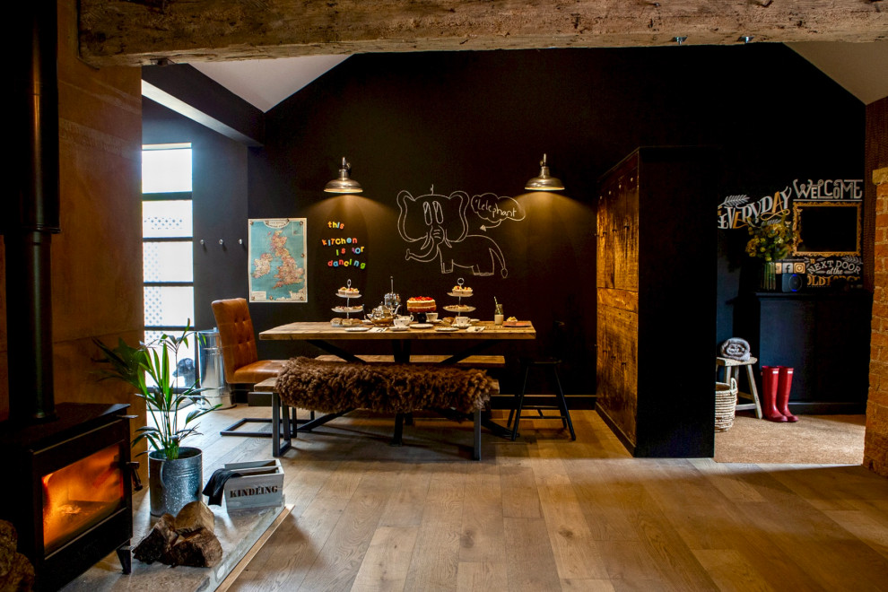 Cette photo montre une salle à manger ouverte sur le salon éclectique de taille moyenne avec un mur noir, un sol en bois brun, un poêle à bois, un manteau de cheminée en métal, un sol marron et un plafond voûté.