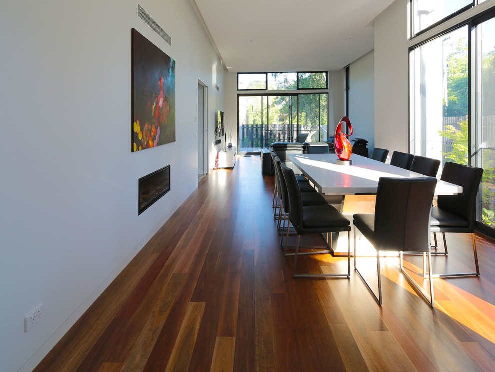 Example of a large trendy medium tone wood floor and brown floor enclosed dining room design in Melbourne with white walls, a standard fireplace and a metal fireplace