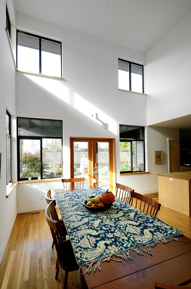 Cette image montre une grande salle à manger ouverte sur le salon minimaliste avec un mur blanc, parquet foncé, aucune cheminée et un sol marron.