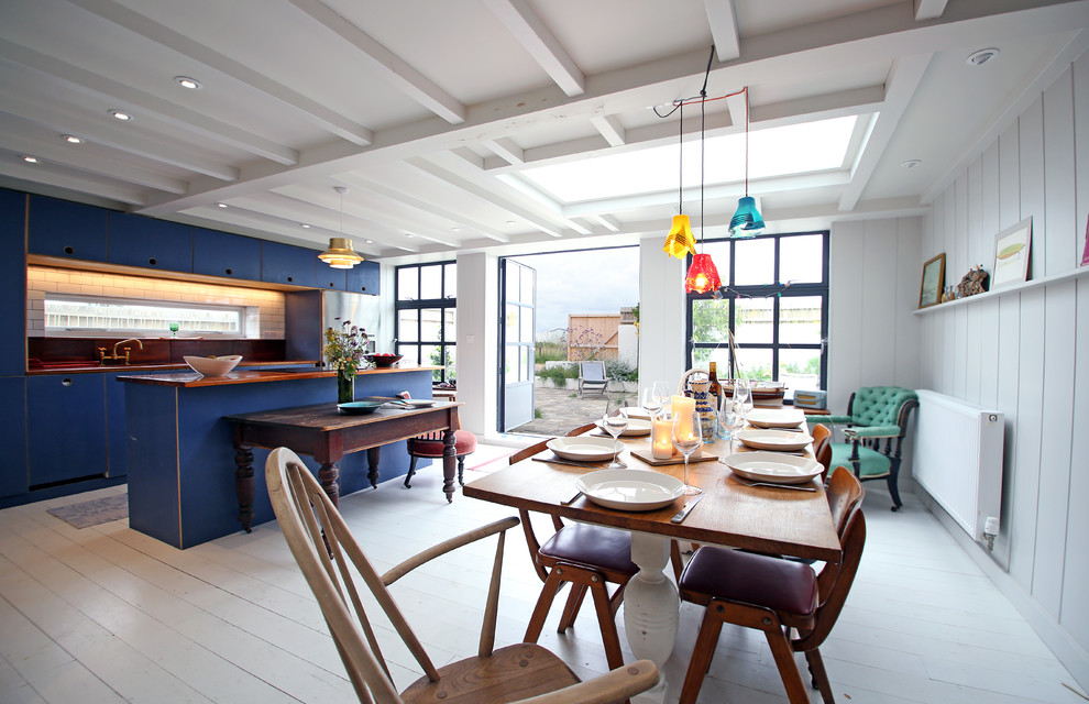 Immagine di una sala da pranzo aperta verso la cucina costiera con pavimento in legno verniciato e pareti bianche