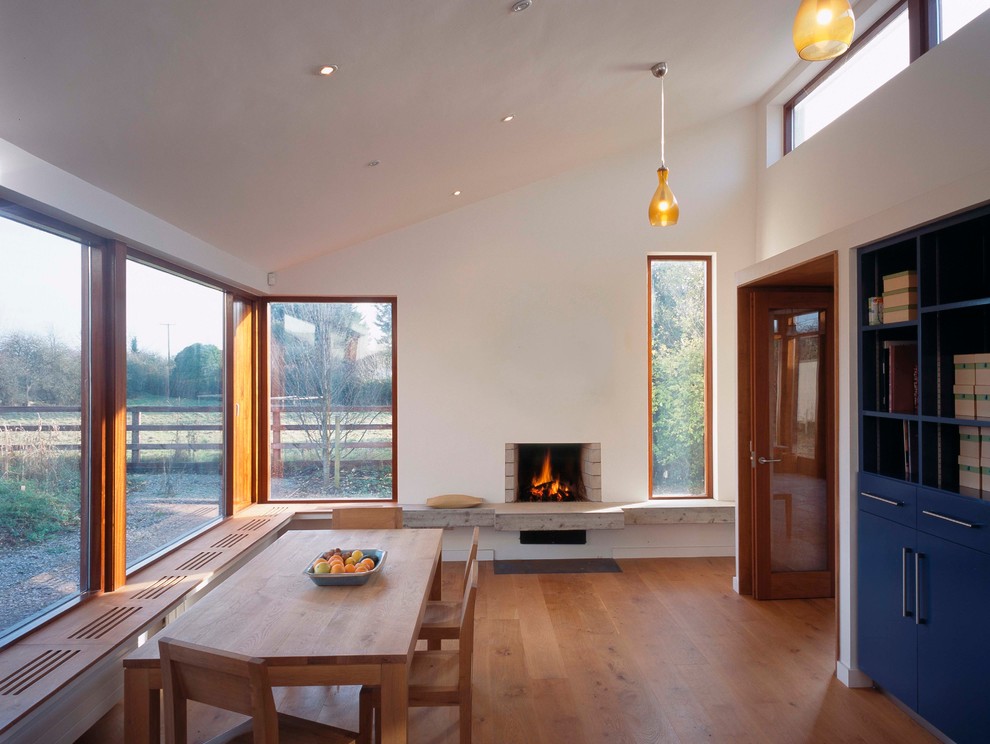Idée de décoration pour une salle à manger design avec un mur blanc, un sol en bois brun et une cheminée standard.